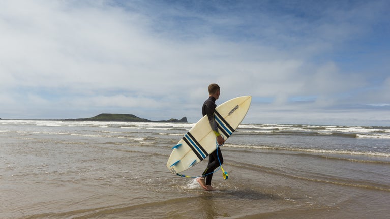 Surfer holding their board on Rhosili beach, Gower Peninsula, Wales